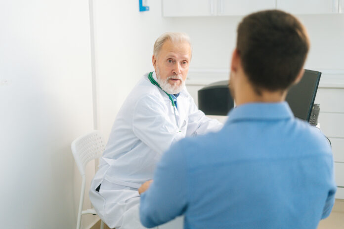 Close-up view from back to mature adult male doctor wearing white coat consulting unrecognizable young man patient about illness or surgery. Jakie ćwiczenia pomagają w leczeniu nietrzymania moczu
